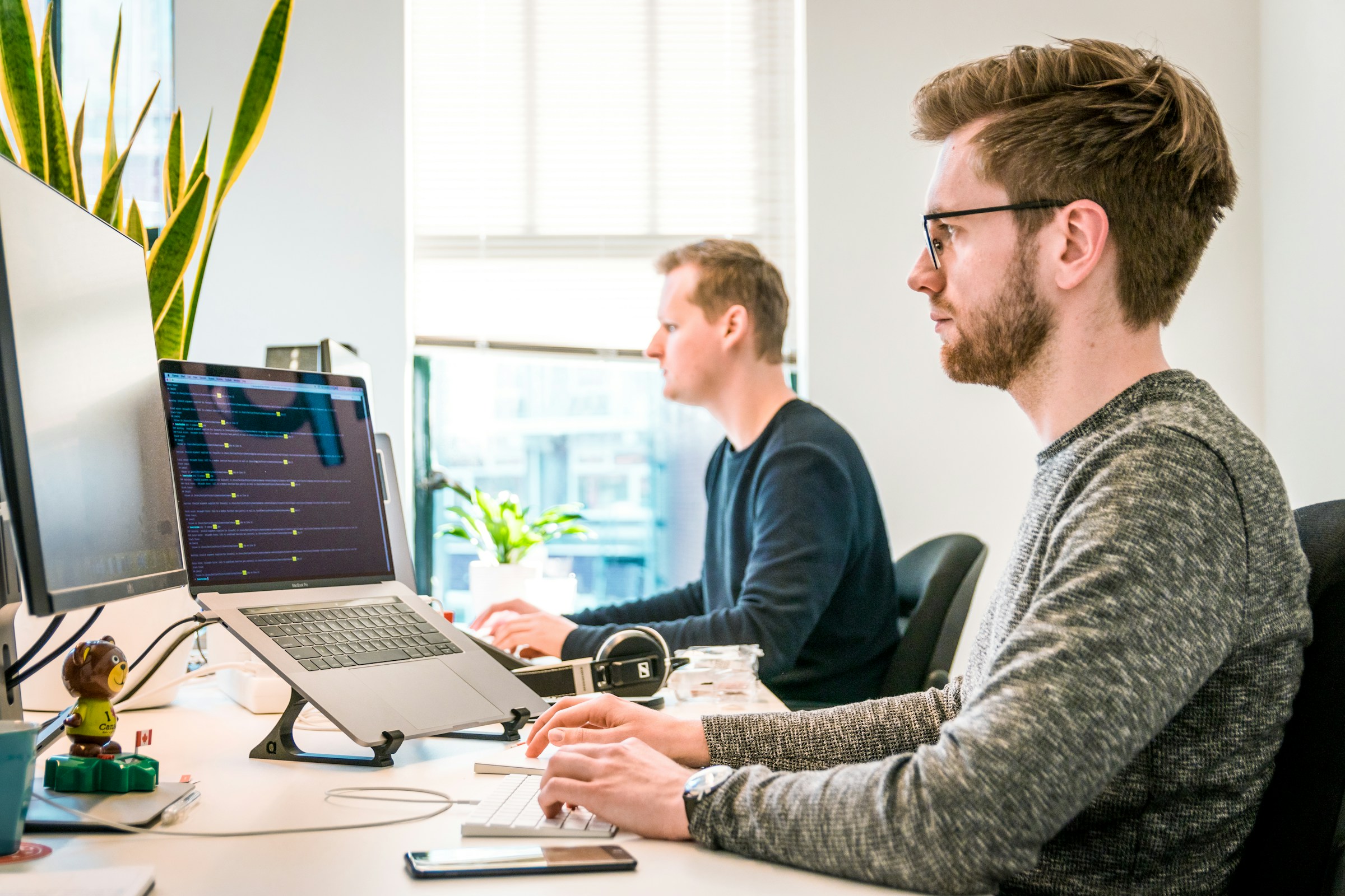 Two team members working at their desks with monitors in a modern office.