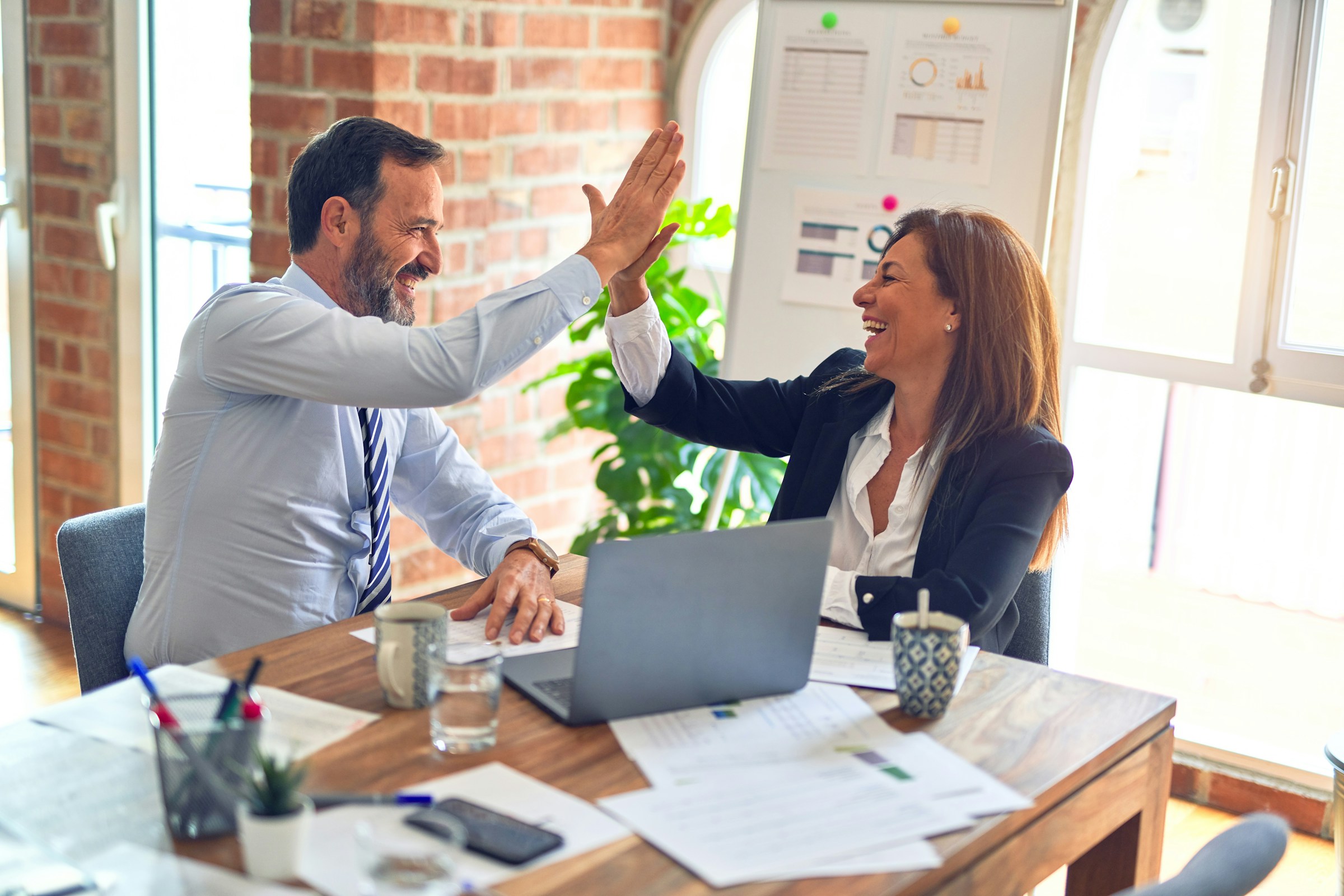 Two business colleagues high-fiving over a laptop, celebrating a sales win.